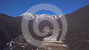 Tourist village in mountain forest valley with view of snow cap. Clip. Tourist town at foot of wooded mountain with snow