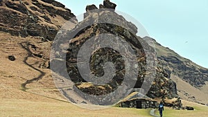 Tourist visit turf house and Drangurinn Rock in Southern Iceland.