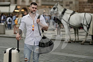 Tourist walking on city street. Traveler with suitcase. Handsome young man on business trip walking with his luggage on