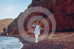 Tourist walking on Red beach on Aegean sea coastline Santorini island, Greece. Woman with backpack traveling