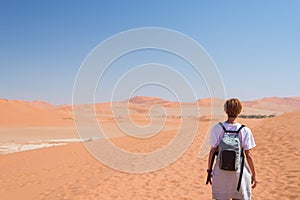 Tourist walking on the scenic dunes of Sossusvlei, Namib desert, Namib Naukluft National Park, Namibia. Adventure and exploration