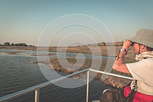 Tourist watching wildlife by binocular while on boat cruise on Chobe River, Namibia Botswana border, Africa. Chobe National Park,