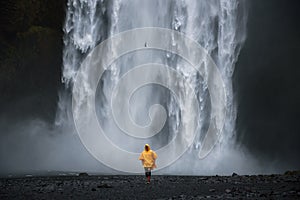 Tourist wearing a yellow raincoat walks from the Skogafoss waterfall in Iceland