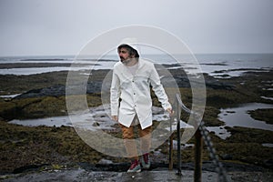 Tourist in white raincoat walks on iceland shore