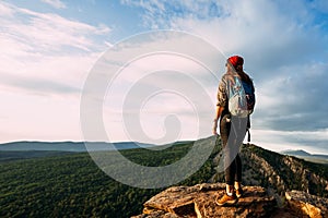 A tourist woman with a backpack admires the sunset from the top of the mountain. A traveler on the background of mountains.