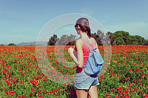 Tourist woman with backpack on the field of red poppies near of Girona, Catalonia, Spain near of Barcelona. Scenic nature