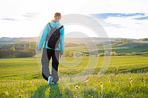 Tourist woman with backpack standing on green grass hill