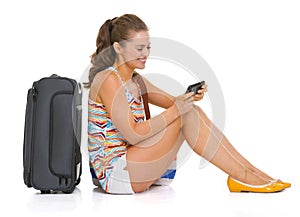 Tourist woman with bag sitting on floor and writing sms