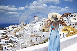 A tourist woman in a blue summer overlooks the beautiful village of Oia