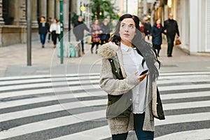 Tourist woman crossing a lost street while consulting a map on her smartphone