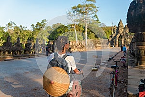 Tourist woman cycling around Angkor temple, Cambodia. Angkor Thom main gate Buddha face sculpure ruins in the jungle. Eco friendly