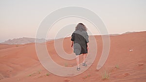 Tourist woman in dress walking along sand dunes in red desert in UAE.