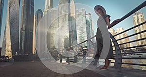 Tourist woman in fashionable summer dress and hat enjoying Dubai marina skyline