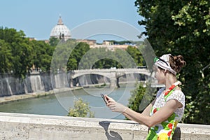 Tourist woman in flower sundress with tablet in hands standing at Rome bridges and masterpiece dome background