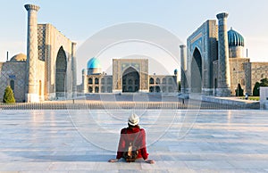 tourist woman with hat and dress red sitting on Registan, an old public square in the heart of the ancient city of Samarkand,