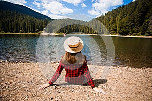 Tourist woman in hat sitting backwards and watching magic lake in mountainous  landscape.