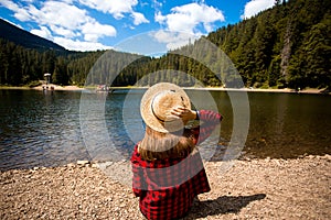 Tourist woman in hat sitting backwards and watching magic lake in mountainous landscape