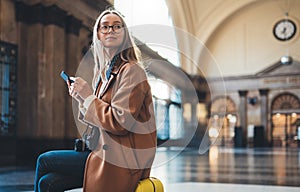 Tourist woman holding mobile phone on platform station in Barcelona. Young girl traveler waiting train using online cellphone