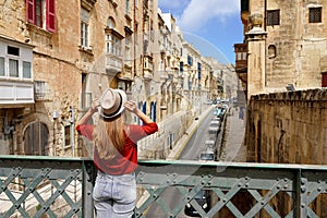 Tourist woman holds hat on iron bridge looking the old town of Valletta, Malta