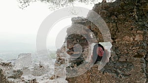 Tourist woman looking around through window ruined buildings in ancient mountain town. Traveling woman walking in