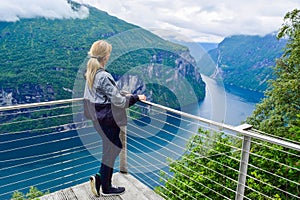 Tourist woman looks at Geirangerfjord and Seven Sisters Waterfall near small village of Geiranger. View from Eagles Road viewpoint