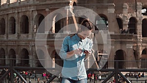 Tourist woman looks at the photos of buildings in her smartphone. Background of Colosseum in Rome, Italy. Slow motion.