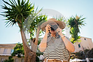 Tourist woman photographer standing under palm tree in old Greek city. Summer vacation concept. Lady exploring island