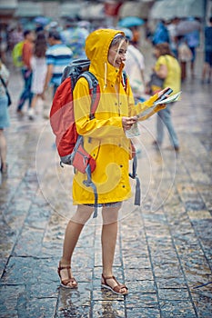 Tourist woman in raincoat, with map and phone on walk thorugh city. Summertime rain. Travel, city, lifestyle concept photo