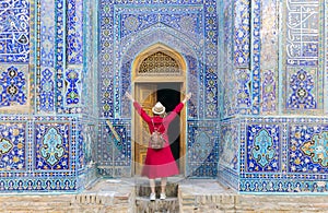 tourist woman in red dress clothes stands near an ancient architectural monument with wooden doors in oriental style with Islamic