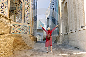 tourist woman in red dress clothes stands in the Shah-i-Zinda Ensemble in Samarkand, Uzbekistan photo