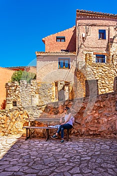 Tourist woman resting on a wooden bench next to the stone houses of the village of Anento, Zaragoza. photo