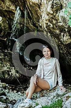 tourist woman sitting on stones in cave with waterfall background
