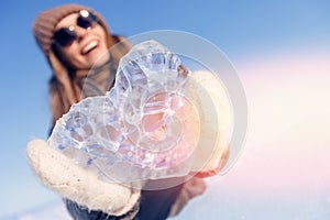 Tourist woman smile in sunglasses holds crystal clear heart ice on background of winter lake Baikal