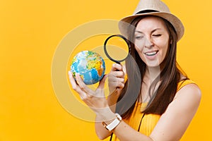 Tourist woman in summer casual clothes, hat looking through magnifying glass on globe isolated on yellow orange