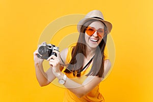 Tourist woman in summer casual clothes, hat take picture on retro vintage photo camera isolated on yellow background