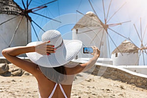 Tourist woman takes a picture of the famous windmills of Mykonos,