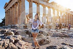 Tourist woman takes selfie photos in front of the Parthenon Temple at the Acropolis of Athens, Greece