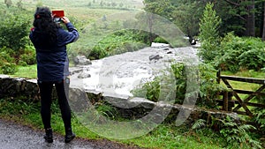 Tourist woman taking pictures of mountain stream in Lake District.