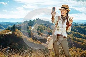 Tourist woman taking selfie with phone and showing victory