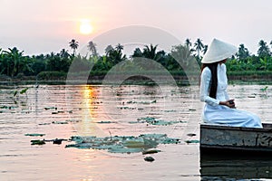 The tourist women wearing white traditional Vietnam dress Ao Wai and Vietnam farmer`s hat and sitting on wooden boat in flower