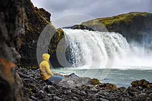 Tourist in a yellow jacket relaxing at the Godafoss waterfall in Iceland