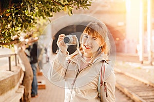 Tourist young girl photographer takes photo on small camera while traveling, smiles and laughs