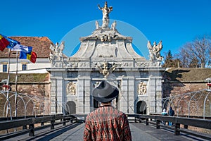 A tourist young man with a hat admiring a fortress gate entrance. A man admiring the 3rd Gate of the Alba-Carolina Fortress in