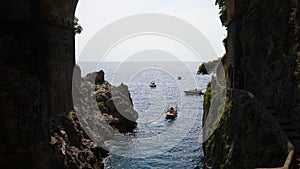 Touristic boat with people passes under Fiordo di Furore Bridge, floats out of bay into Mediterranean sea on sunny