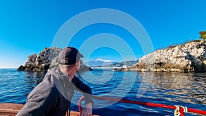 Touristic man on boat with panoramic view from open sea on snow capped volcano Mount Etna in Taormina, Sicily, Italy, Europe, EU.