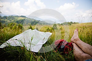 Touristic trails map on green summer grass near hiker legs resting on backpack