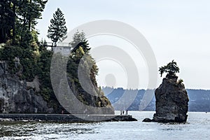 Touristis at siwash rock on stanley park seawall and cliff on a sunny summer day