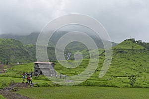 Tourists around a house with green mountains river flowing under fogy clouds in Ashane, India