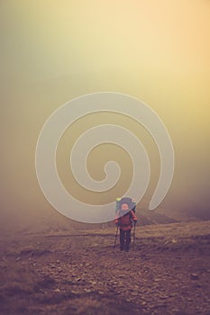 Tourists with backpacks climb to the top of the mountain in fog.