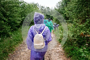 Tourists with backpacks in raincoats go along the road to the mountains. Travel concept, leisure activity, vacation